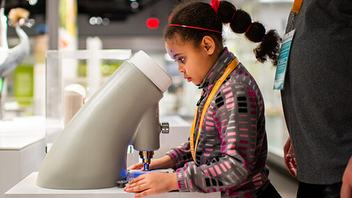 Young girl looking into a microscope in the Cherish Nebraska exhibit