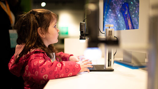 Young girl looking at an object under a microscope in the Cherish Nebraska exhiit