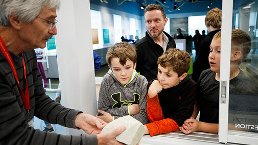 Young kids and their dad learning from a paleontologist in the visible lab