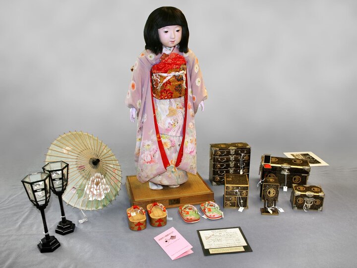 A Japanese Friendship Doll in kimono surrounded by accessories like a trunk, shoes, and passport. 