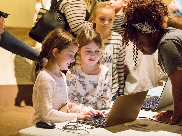 Two young girls look at a display on a laptop during a membership drive.