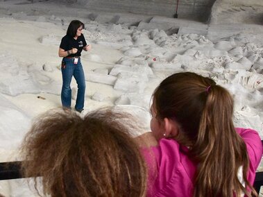 Kids on boardwalk watching researcher talk from the digsite