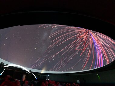 A spray of red and green lasers flow across the planetarium fulldome.